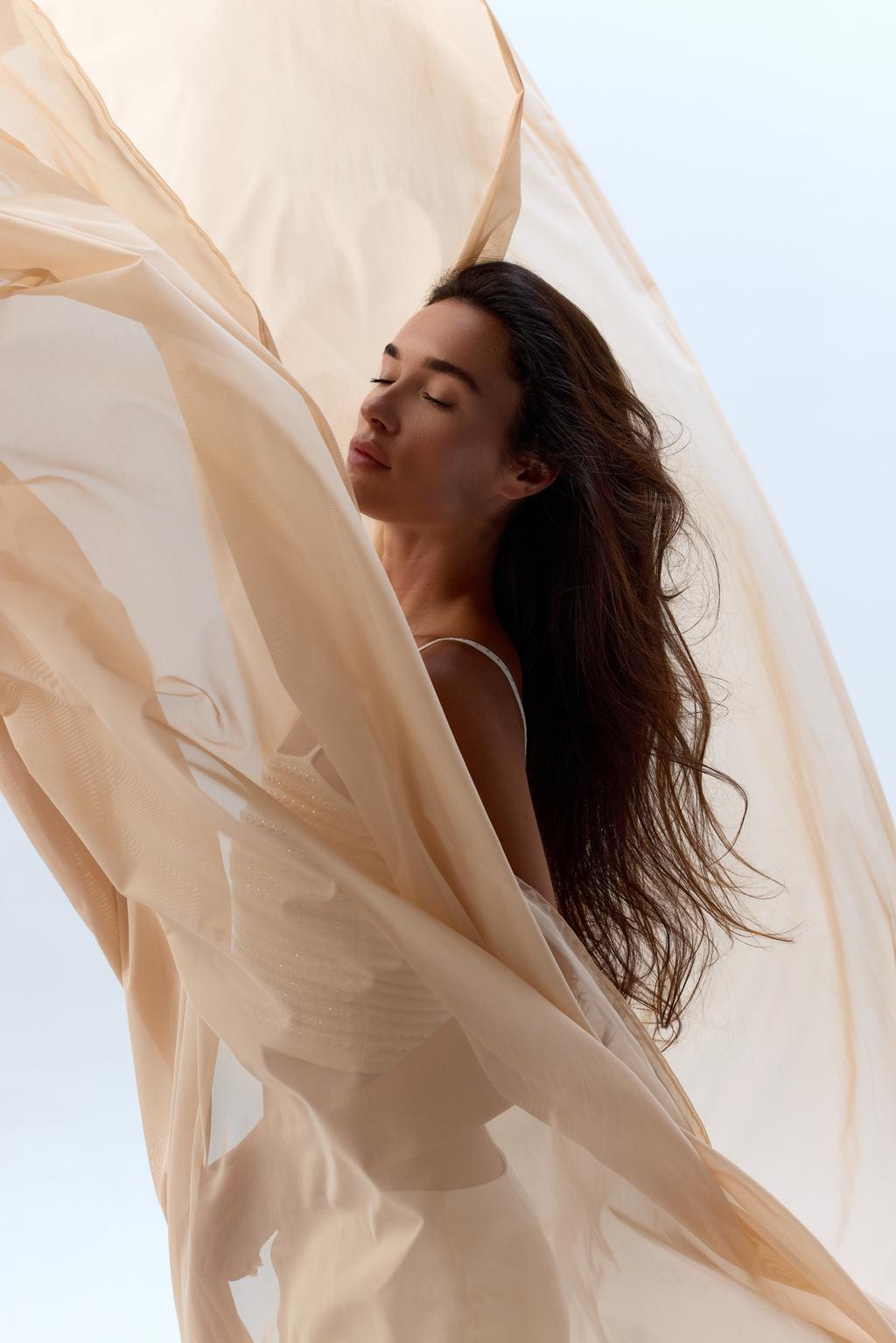 Une femme, les yeux fermés, dans un voile de tissu léger